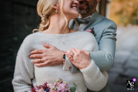   The married couple stands closely together at Schloss Heeren in Kamen, Germany, showcasing an intimate embrace with the focus drawn to their intertwined hands and wedding rings.
