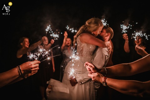   Surrounded by glowing sparklers at Schloss Heeren in Kamen, Germany, the newly married couple embraces, with friends and family creating a circle of celebration and light around them.