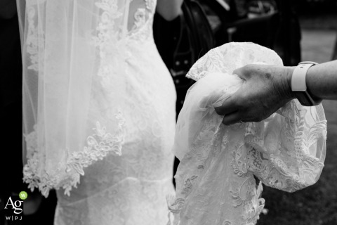 Bride’s Wedding Dress Held And Lit by Gentle Light at Saint Mary’s on the Hill in Wednesbury, UK A wedding dress hangs in a hand in the gentle light at Saint Mary’s on the Hill Catholic Church, Wednesbury, UK, its elegant details of the bride’s special day.
