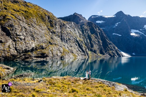 At Lake Erskine in Queenstown, New Zealand, dramatic mountains and cliffs surround the couple during their private shoreline wedding ceremony, creating a breathtaking setting that emphasizes both intimacy and scale.