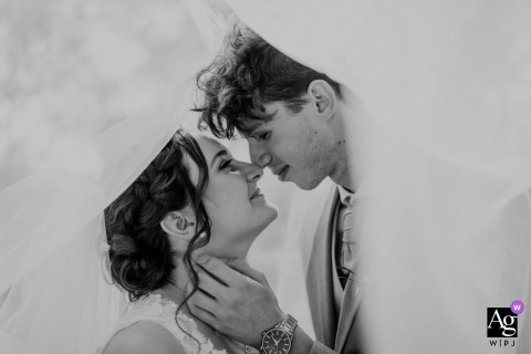 At the reception venue in Budapest, Hungary, the bride and groom share a quiet black-and-white portrait beneath the veil, gently touching noses in an intimate moment that draws all attention to their connection.