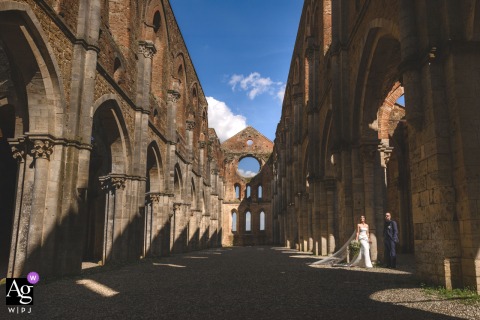 Historic Architecture Frames The Couple At San Galgano Abbey In Tuscany, Italy Beautifully At San Galgano Abbey in Tuscany, Italy, the bride and groom share a timeless portrait surrounded by the abbey's remarkable architecture, creating an elegant image that blends romance with the grandeur of the historic setting.