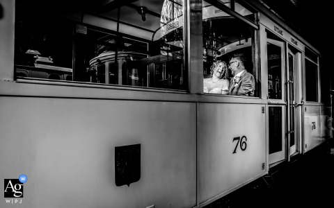 At a tram location in Gelderland, the Netherlands, the bride and groom share a playful black-and-white portrait while riding together, turning an ordinary journey into a joyful wedding-day moment filled with personality.