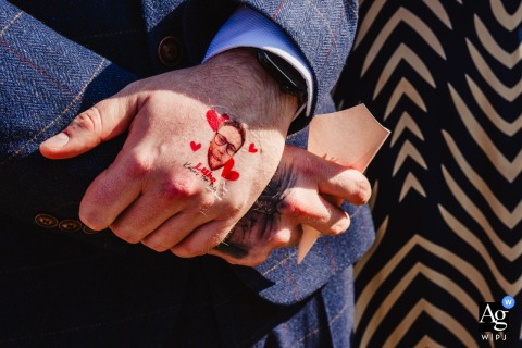 At Moat Hall Barns in Shropshire, UK, a groomsman proudly holds a confetti cone while showing off his temporary tattoo, creating a lighthearted wedding-day moment filled with personality and playful anticipation.