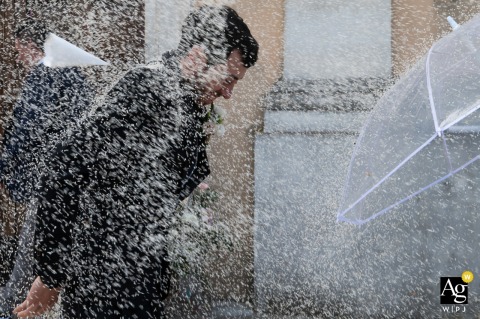 At the Church of San Prospero in Suzzara, Mantova, Italy, the groom hurries toward an umbrella, realizing just a moment too late that the rain is about to arrive, creating a humorous and perfectly timed wedding-day image.