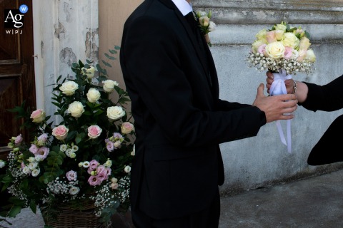 At the Church of San Prospero in Suzzara, Mantova, Italy, a close detail captures the bride handing her bouquet to the groom, highlighting both the meaningful exchange and the floral design the couple chose to complement their wedding ceremony.