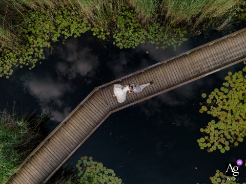 In Sursee, Switzerland, a drone captures the bride and groom lying on their backs on a pedestrian bridge, looking upward together as the elevated view turns the walkway into a clean, graphic wedding portrait.