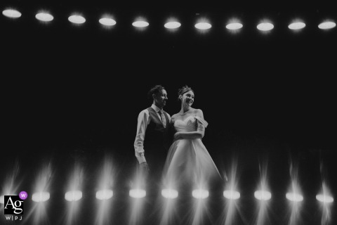 At Domaine de la Brosse Montmort in France, the bride and groom share a black-and-white nighttime portrait beneath a row of glowing light fixtures, with their reflections mirrored along the bottom of the frame to create a striking, symmetrical composition