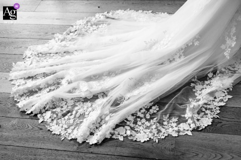 At Château d'Arcelot in France, the bride's wedding dress train is photographed in black and white, emphasizing its flowing lines, rich texture, and timeless elegance through a refined detail image.
