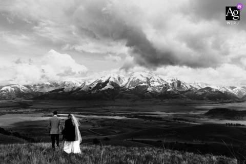 In Paradise Valley, Montana, the bride and groom walk together beneath dramatic clouds, with sweeping mountain views creating a striking backdrop for their wedding-day portrait.