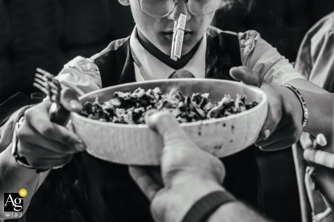 At The Fish Pond in Matlock Bath, England, a young boy humorously wears a clothespin holding the wedding details on his nose while happily accepting a plate of food, creating a playful and memorable reception moment.