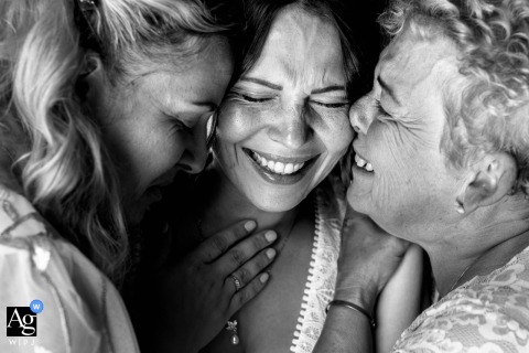 At La Pierre à Sel in France, the bride shares a joyful embrace with her sister and mother in a tightly framed black-and-white photograph, capturing their smiles and the warmth of this intimate moment.