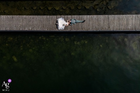 At Lake Zug, Switzerland, a drone captures the bride and groom lying on a wooden dock, with the still water below creating a clean, minimalist composition that emphasizes their connection.