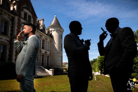 At Château de la Pouyade in Charente, France, the groom stands in the light while his two groomsmen, each holding a cigar, remain in shadow as silhouettes, creating a dramatic and stylish wedding-day portrait.