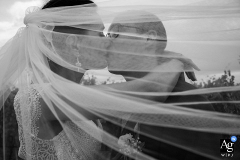 At Domaine de la Clausade in France, the bride and groom share a kiss beneath a sweeping veil in a black-and-white portrait, creating a timeless image filled with elegance, movement, and intimacy.