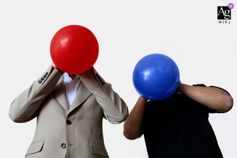 At the groom’s home in Zhanjiang, Guangdong, China, the groom and his groomsman take part in a balloon-blowing wedding game, with oversized balloons covering their faces and creating a delightfully humorous scene.