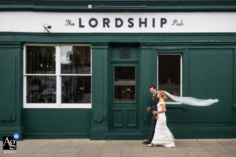 Outside The Lordship Pub in Dulwich, London, England, the bride and groom walk together in front of the venue, creating a relaxed and natural wedding-day portrait.