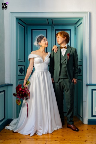Beneath the blue doors of Château Lacoste, the bride and groom exchange an elegant glance, framed by soft light and rich wedding colors in a quiet moment before their celebration begins.