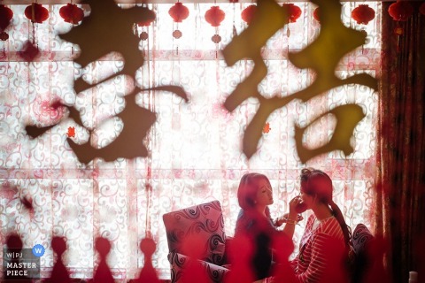 The bride can be seen getting her makeup done in this photo taken through a curtain by a Shanxi, China wedding photographer.