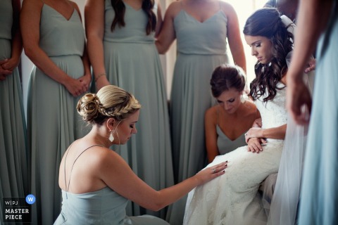 The bride is surrounded by her bridesmaids, one of whom touches her lap in this photo by a Denver, CO wedding photographer.