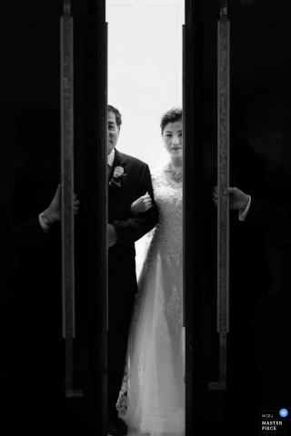 Le photographe de mariage de Shanghai a capturé cette image en noir et blanc des portes de l'église s'ouvrant et révélant le premier aperçu de la mariée avant qu'elle ne se promène