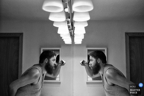 Black and white photo of a man looking at his reflection in the mirror as he gets ready by a Lake Tahoe, CA wedding photographer.