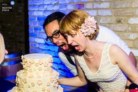 The bride and groom, mouths wide open lean towards their wedding cake in this indoor picture, Let them eat cake in Austin, Texas