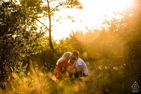 Engagement portrait photo of a couple sitting in a sun drenched grassy field while kissing in the Czech Republic