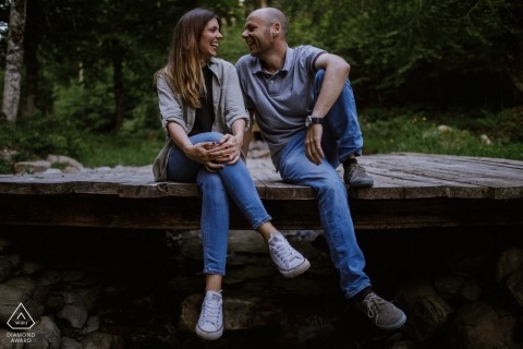 The Zaragoza engaged couple laugh and hang out seated on a wooden footbridge in the midst of a forest