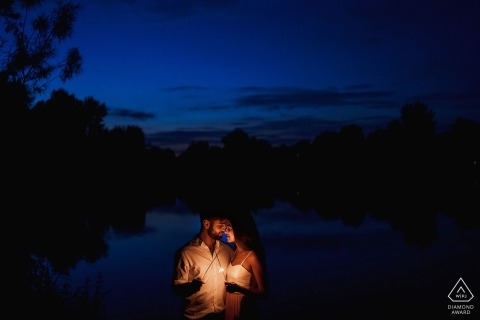 A couple holds a small light as they stand together at night in London during their pre-wedding shoot by an England photographer.