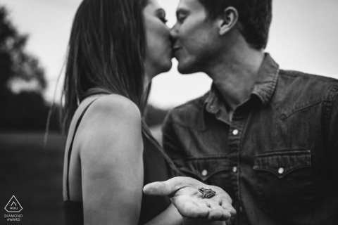 A woman in Edmonton holds a frog as she and her fiance kiss in this black and white engagement portrait by an Alberta, Canada photographer.