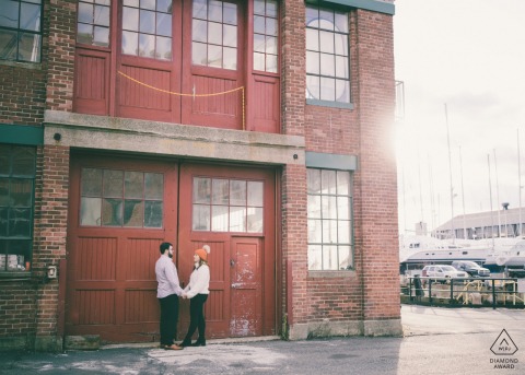 Engagement Session - The couple stands in front of the industrial-cool buildings of the East Boston Shipyard 