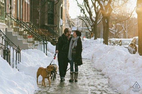 Albany, New York engagement portrait session of a happy couple walking arm in arm with their two dogs down a snowy city sidewalk. 