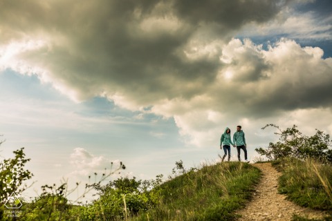 A Brno couple walk on the hill during a rural engagement shoot under the clouds