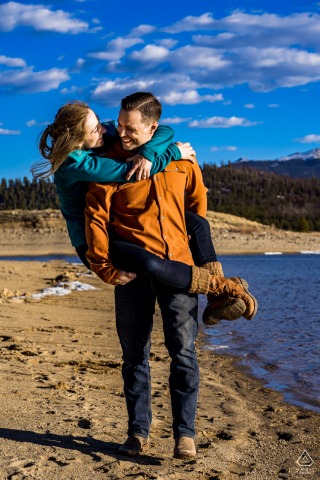 Adventurous, outdoor Twin Lakes, Colorado engagement image of a piggyback couple on mountain lake shore