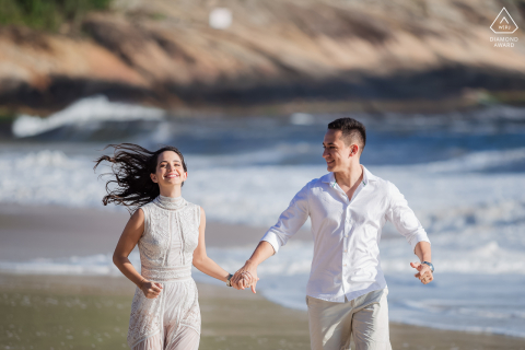 Scenic Rio de Janeiro pre wedding portrait shoot of the young Brazil couple running hand in hand on the beach at the ocean