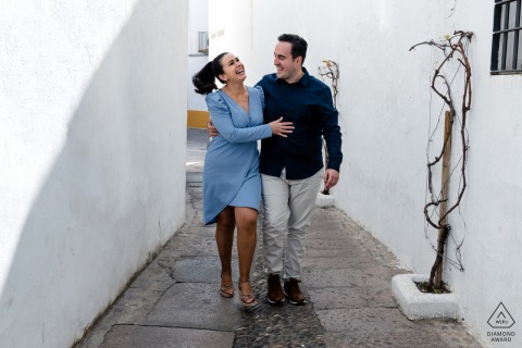 Cordoba post proposal photography showing a smiling Andalusia couple walking through the white painted wall alley
