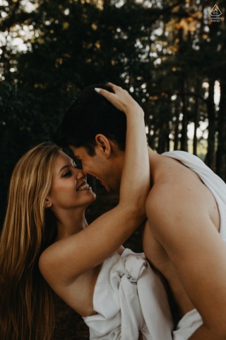 Assis Chateaubriand Engagement. A young Parana couple posing during a pre wedding portrait session while smiling together in sheets outdoors in nature