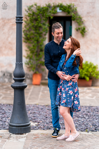 A Grado couple with style and class poses for Italy engagement announcement portraits next to an urban streets lamp post