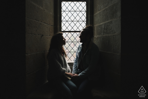 A Mont Saint Michel modern couple poses in window light for an announcement portrait of their Normandy engagement