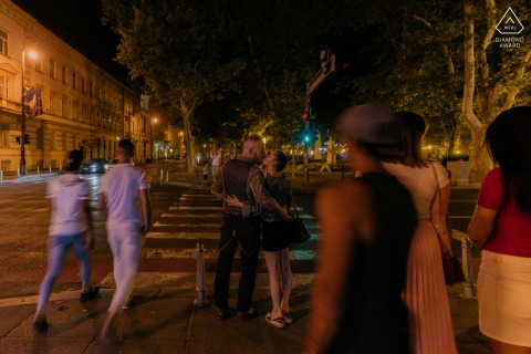 Fotografía de compromiso de estilo de vida de Zagreb de una pareja croata besándose por la noche en las calles con la multitud un desenfoque de una velocidad de obturación lenta