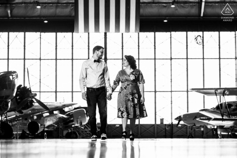 A Wings Over the Rockies Air Museum engagement picture in BW for a Denver, CO Couple walking in an airplane hangar with vintage airplanes around