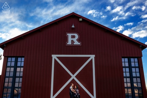 At a rustic local park in Denver, Colorado, a wide angle photo of a couple embracing in front of a red barn, and the R happens to be their last name initial