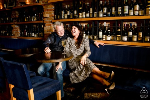 An engaged couple posed for a save-the-date wedding announcement at Plonk Wine Bar in downtown Bozeman, MT, laughing and enjoying their date