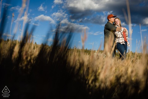 Das Paar kuschelte sich in hohes trockenes Gras und Abendsonne am Dillon Reservoir in Dillon, Colorado, für ihr Save-the-Date-Hochzeitsanzeigebild