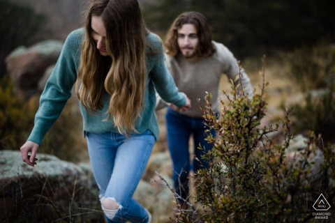 A couple hike for their save-the-date wedding announcement picture while climbing a narrow trail and holding hands on private land in Florissant, CO