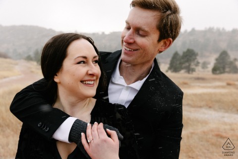 The couple cuddled in Ute Valley Park, Colorado Springs, surrounded by a winter snowstorm and dry grass for an engagement portrait