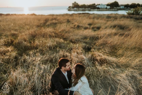A couple is sitting in a grass field in Talmont, France, capturing their love and joy in a beautiful engagement photo session