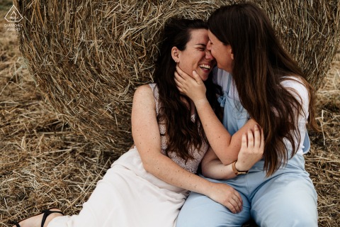 A couple in a rural area near Chartres is captured embracing in an engagement portrait, with a large round bale of hay serving as the backdrop