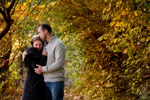 À St Albans, Hertfordshire, ce portrait romantique capture un couple blotti dans leurs manteaux d'hiver, créant une atmosphère chaleureuse dans le magnifique tunnel des arbres automnaux. Prise par un talentueux photographe de mariage du Hertfordshire.